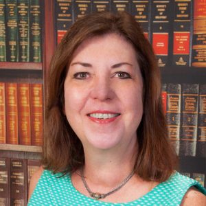 Headshot of Sarah E. Sholes, Esq., founding partner in front of bookshelf filled with law books.